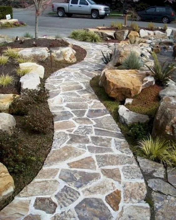 Front yard flagstone path edged with large tan boulders and grasses