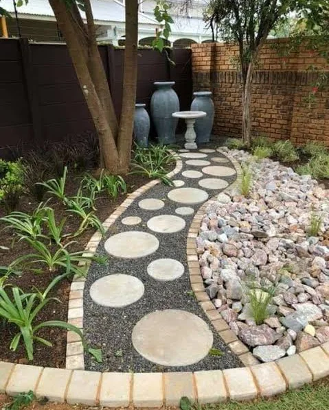 Curved path of round stepping stones in black pebble beside a bed of red pebble