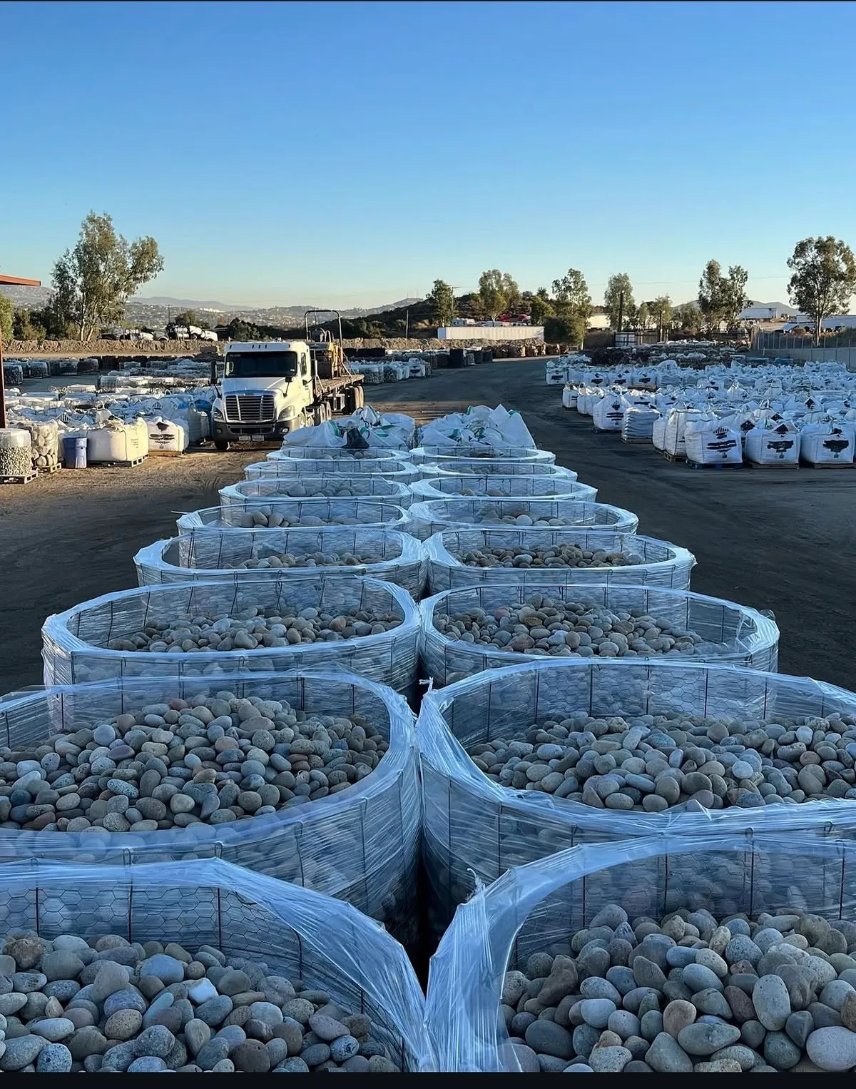Rows of wire baskets full of beach pebble in our stone yard, a flatbed truck behind them